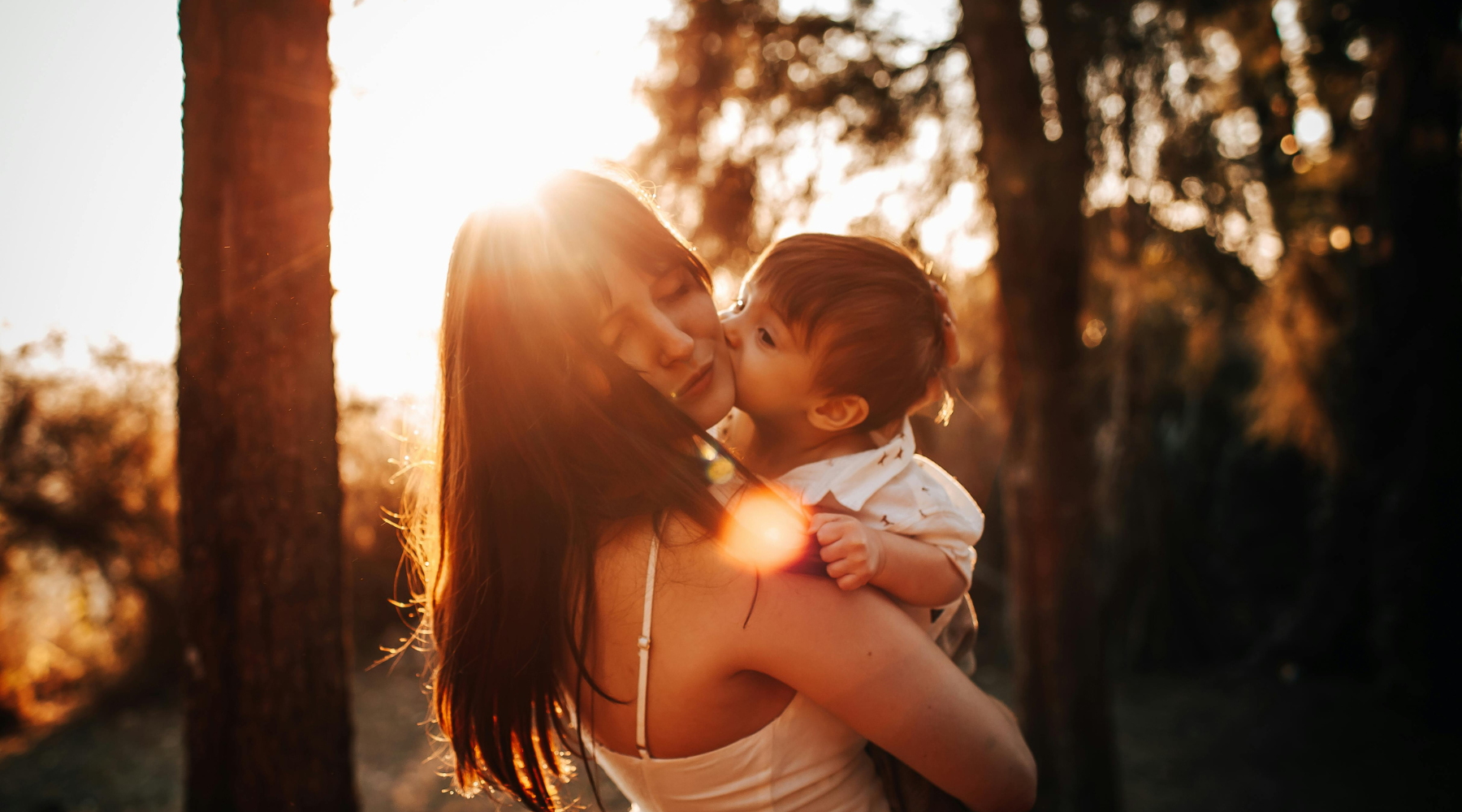 Silhouette of a mother and toddler embracing at sunset to represent family wellness, natural circadian rhythms, and the biological transition from day to night.